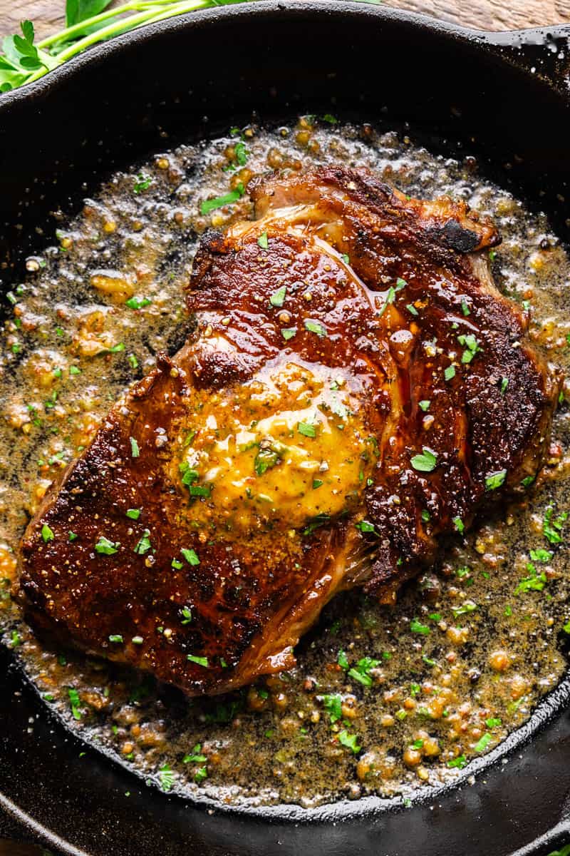 An overhead view of a steak in a skillet with cowboy butter melting all over the top.