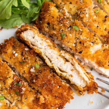 A close up overhead view of a sliced chicken cutlet on a dinner plate with a salad on the side.