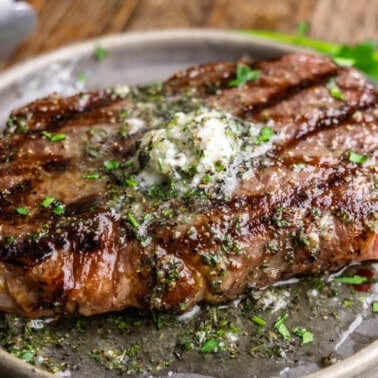 A perfectly grilled steak on a gray plate with resting butter melting on top.