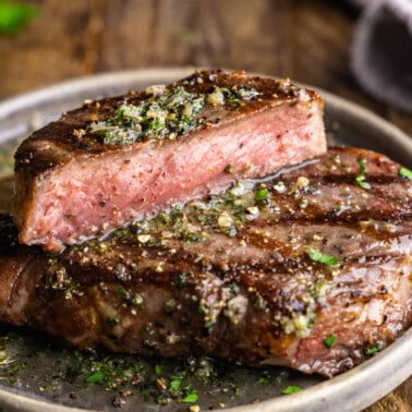 A close up view of a grilled steak on a plate that has been cut in half revealing a perfectly pink and juicy interior.