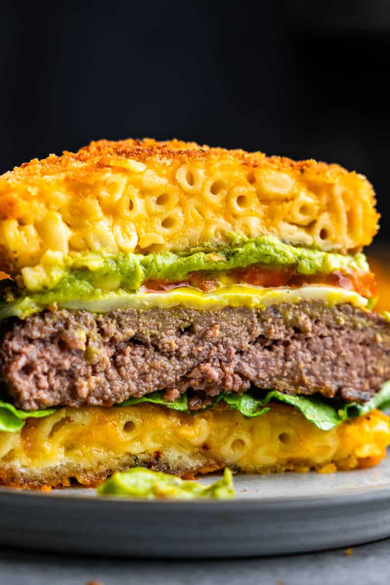 A close up view of a burger that has been cut in half to reveal the instead of a bun made out of bread, it is made out of fried mac and cheese. 