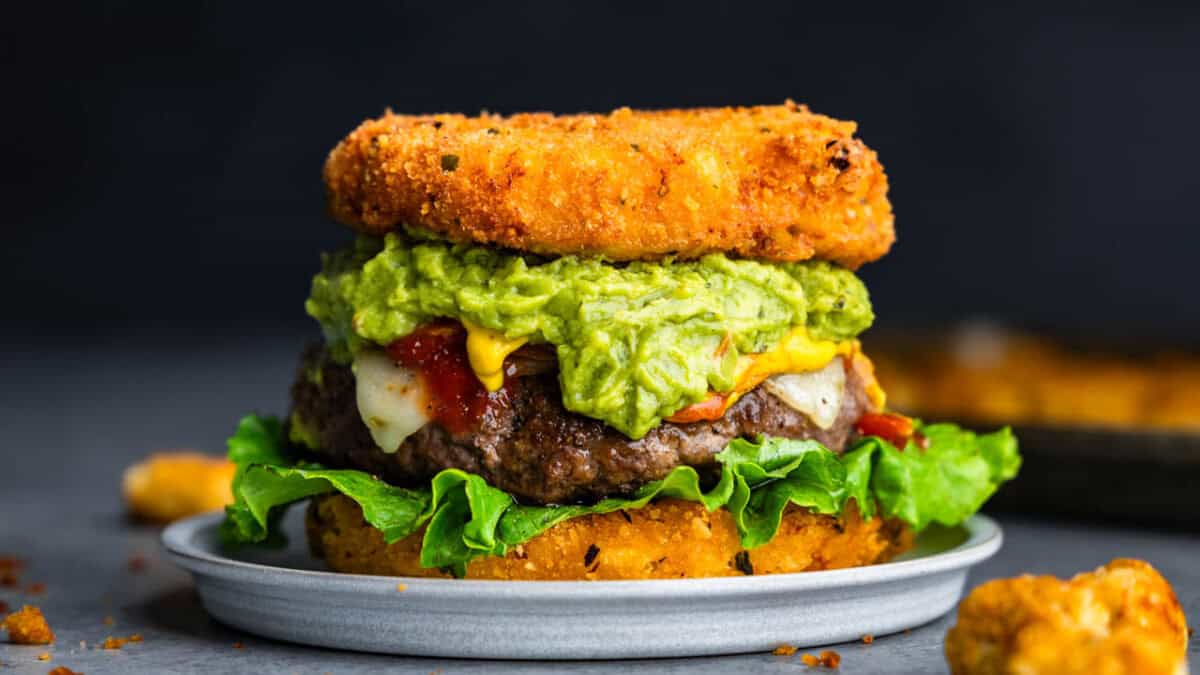 A close up view of a burger topped with guacamole where the buns are made from fried mac and cheese.
