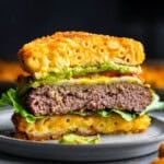 A burger sitting on a gray plate. It has been cut in half to reveal that the burger bun is made from fried mac and cheese.