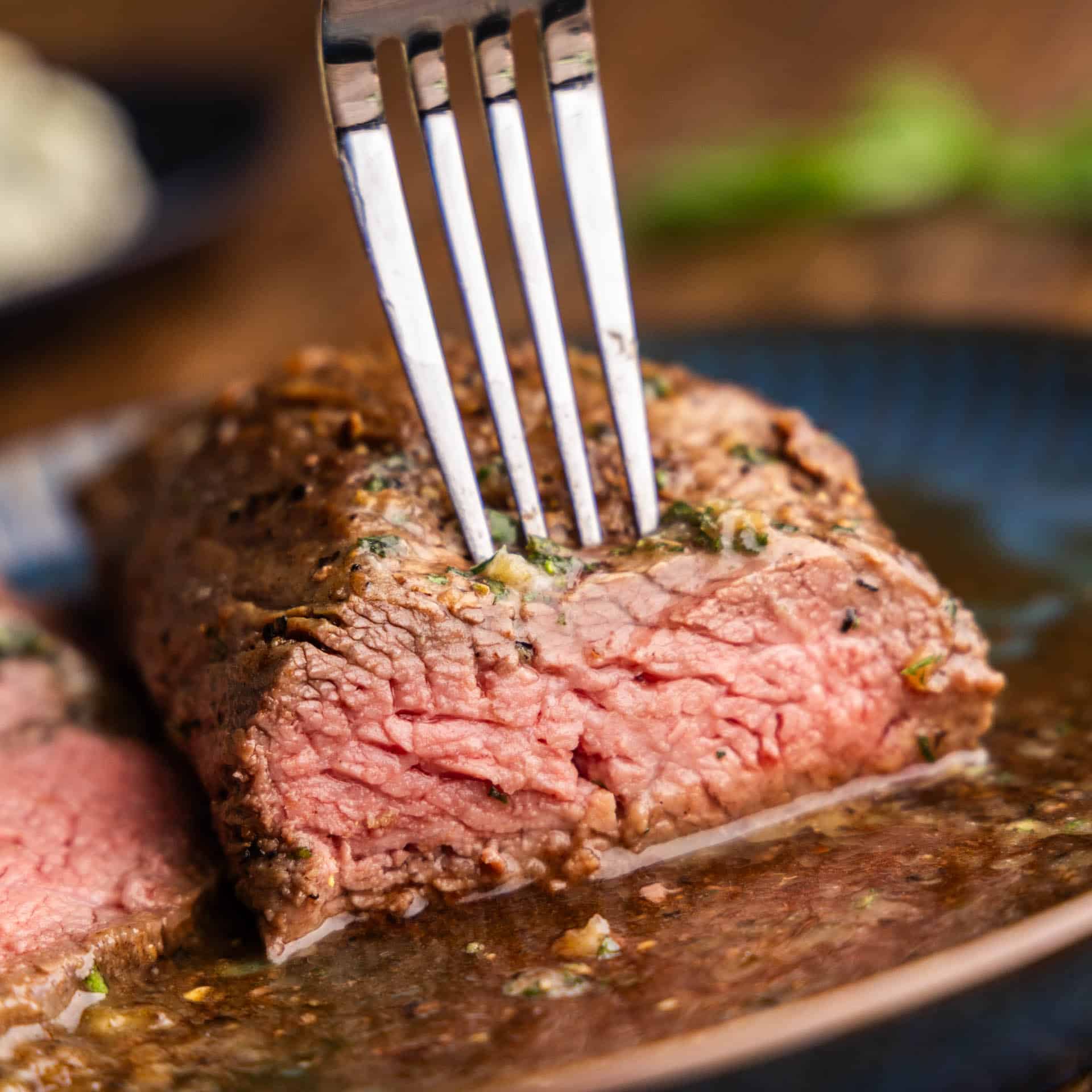 A close up view of a petite tender steak that has already been cut into showing a perfectly pink interior with a fork poking in the top to pick up a piece.