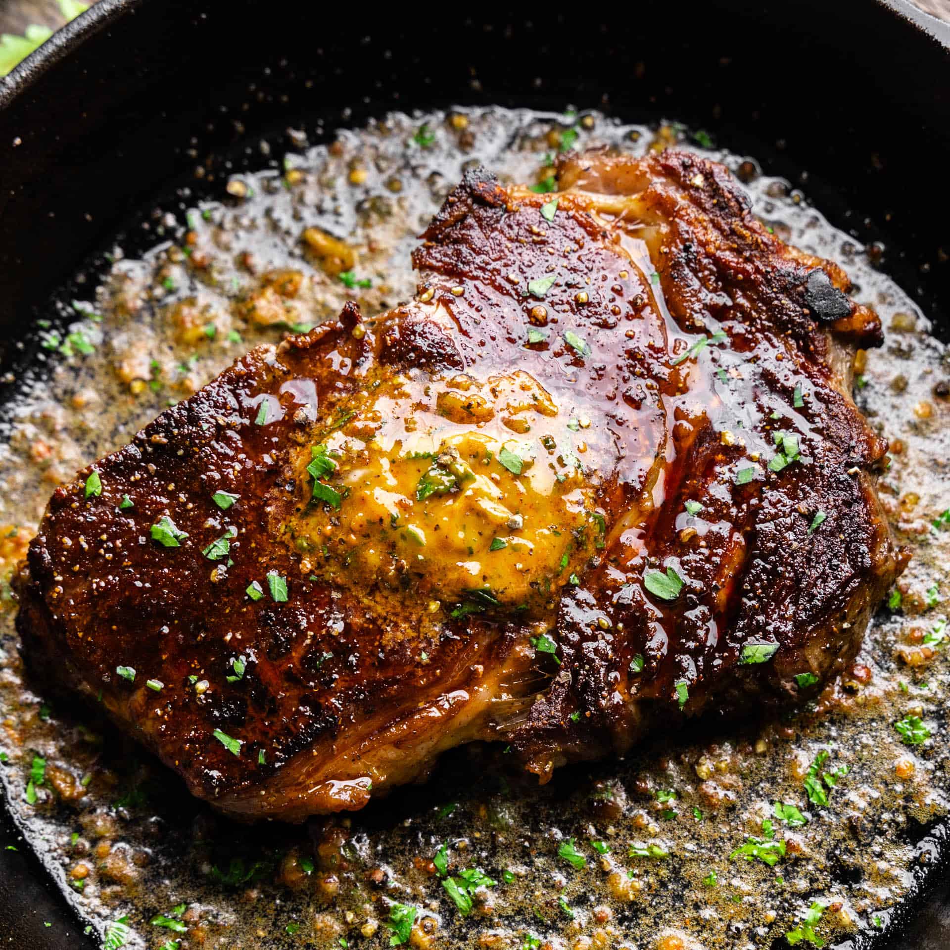 An overhead view of a ribeye steak in a skillet topped with resting butter.