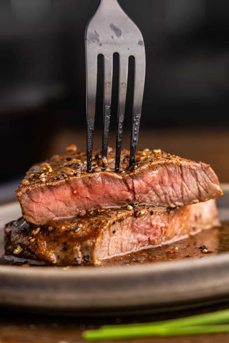 A close up view of a sirloin steak that has been cut in half and stacked with a fork sticking in the top piece.