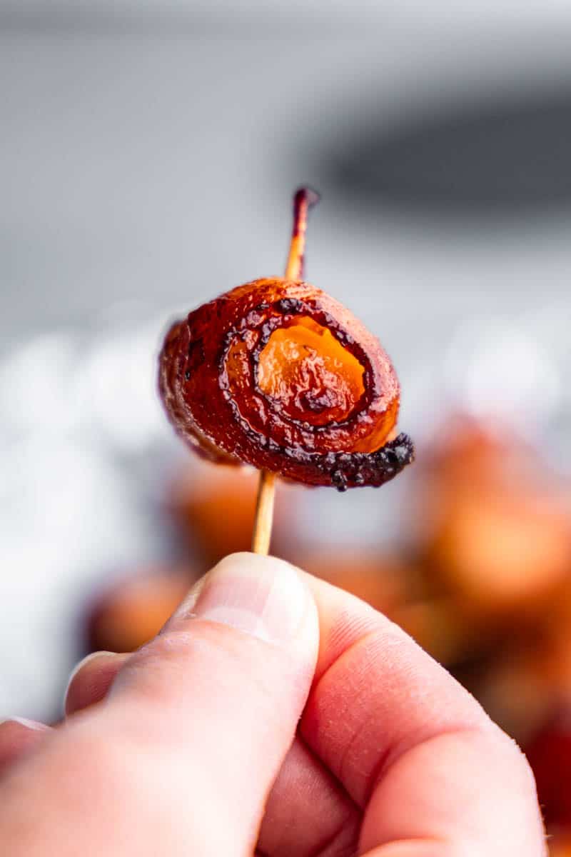 A close up view of someone holding up a bacon wrapped water chestnut on a toothpick. 