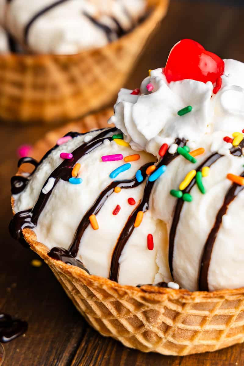 Close up view of a waffle cone of ice cream with sprinkles, chocolate candies and cherries. 