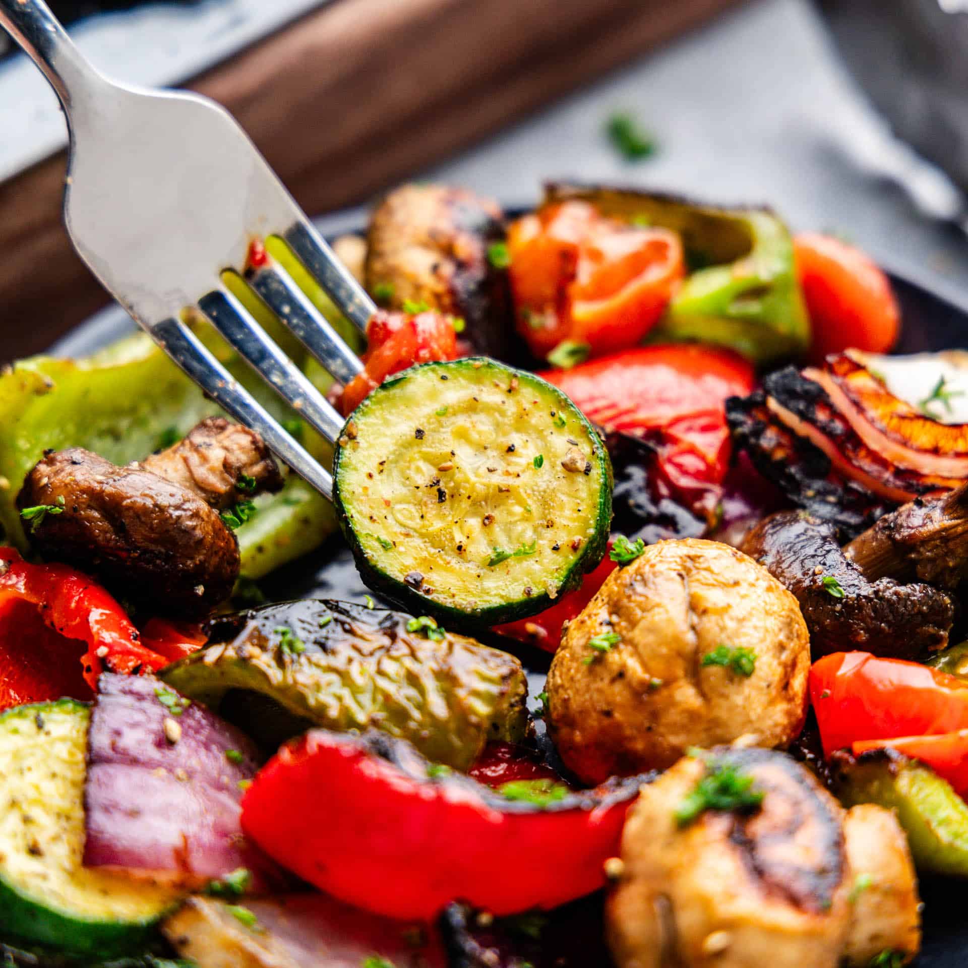 A close up view of a fork lifting out a bite of grilled vegetables from the pan.