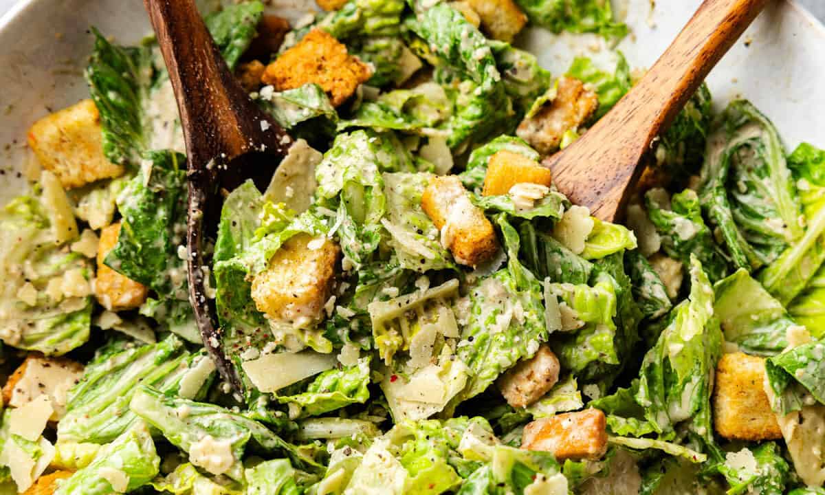 A large bowl of Caesar Salad with a wooden spoon.