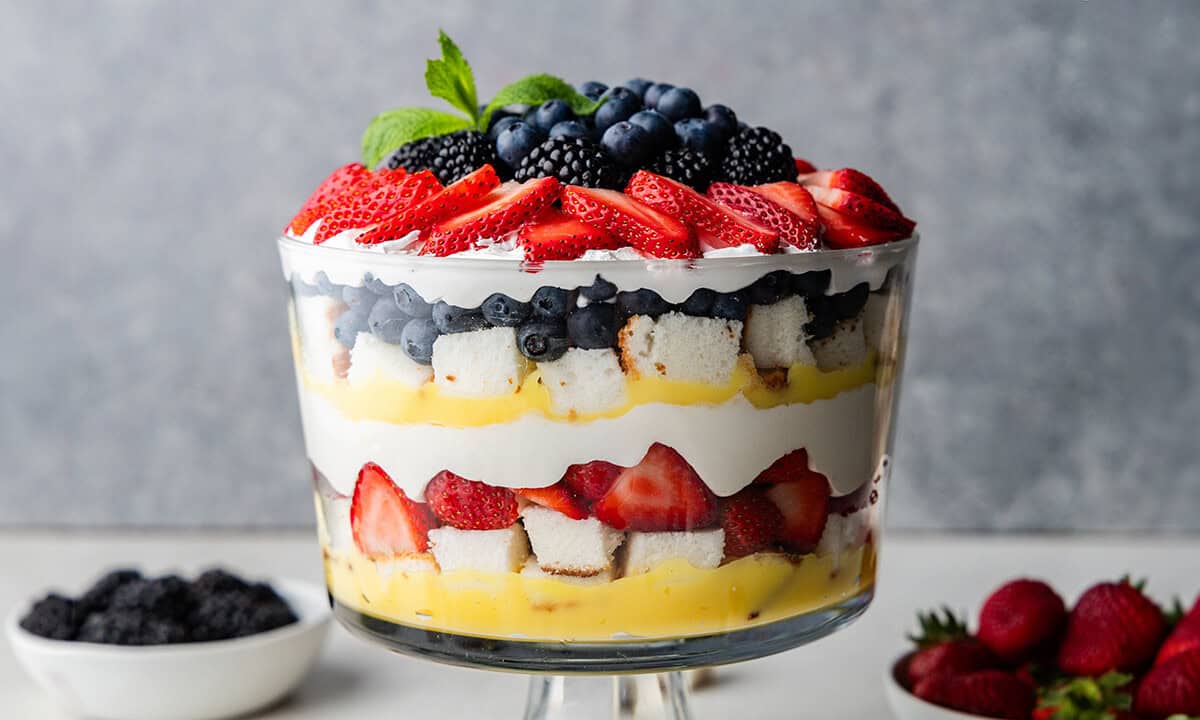 A side view of the creamy berry trifle with bowls of blueberries and strawberries.