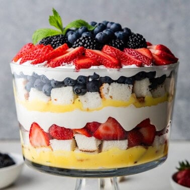 A side view of the creamy berry trifle with bowls of blueberries and strawberries.