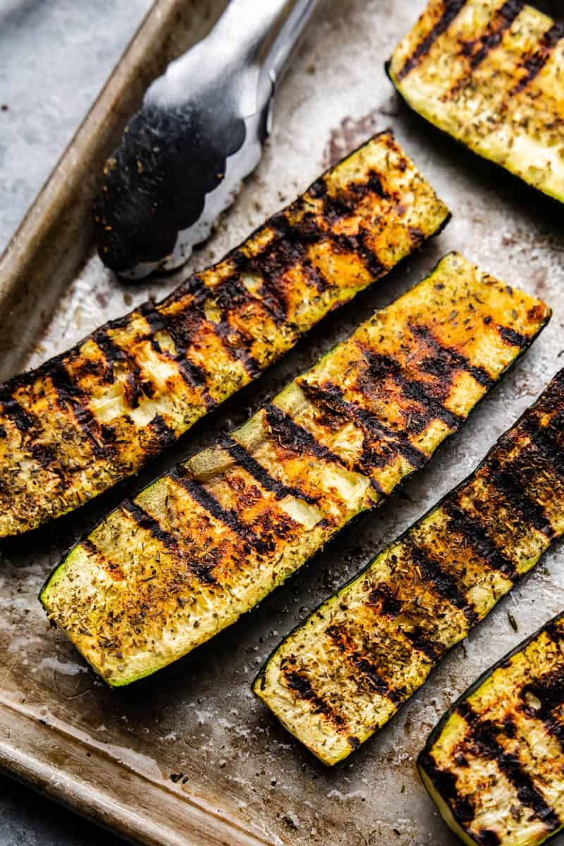Three grilled zucchini laid out on a tray. 