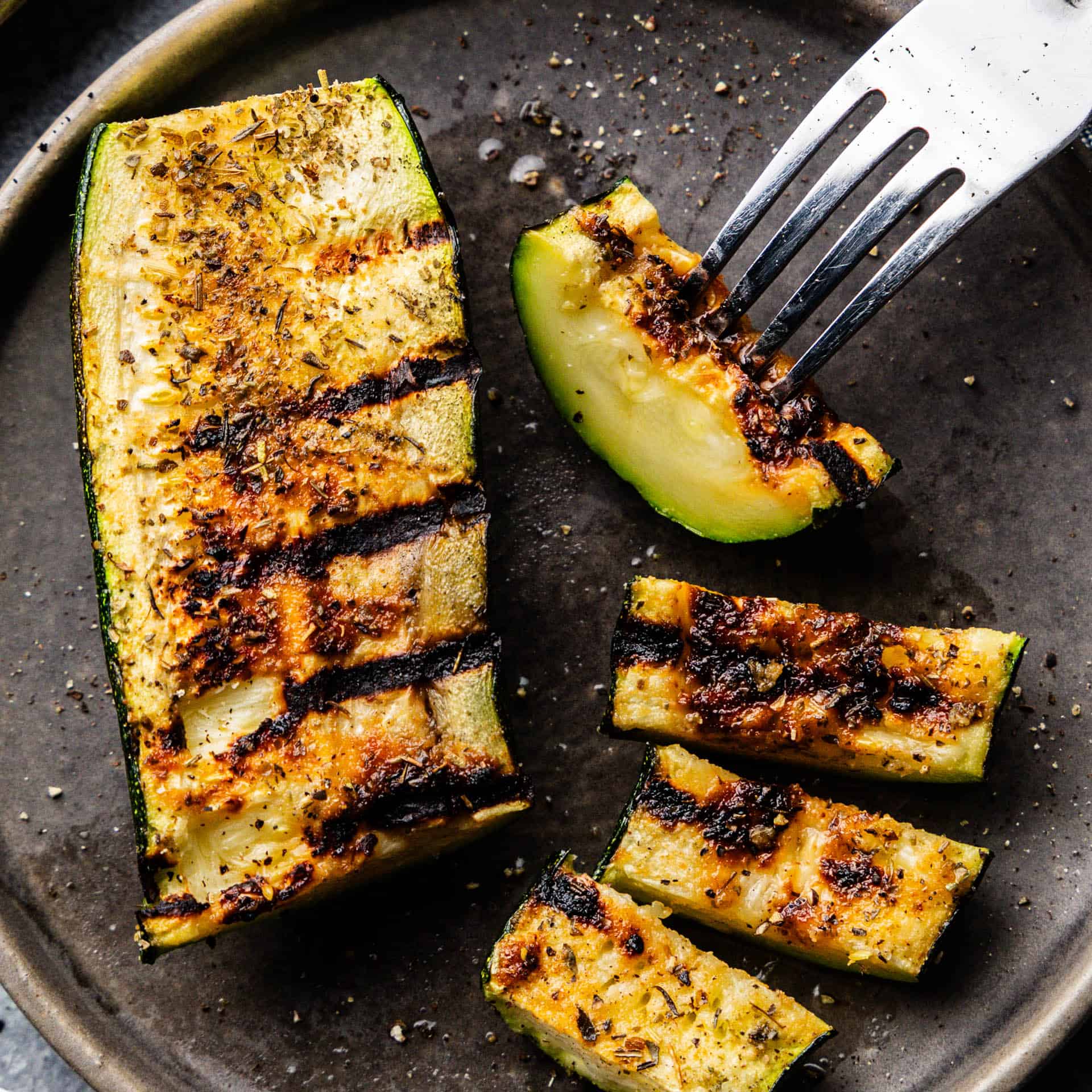 Two slices of grilled zucchini on a plate with a fork.