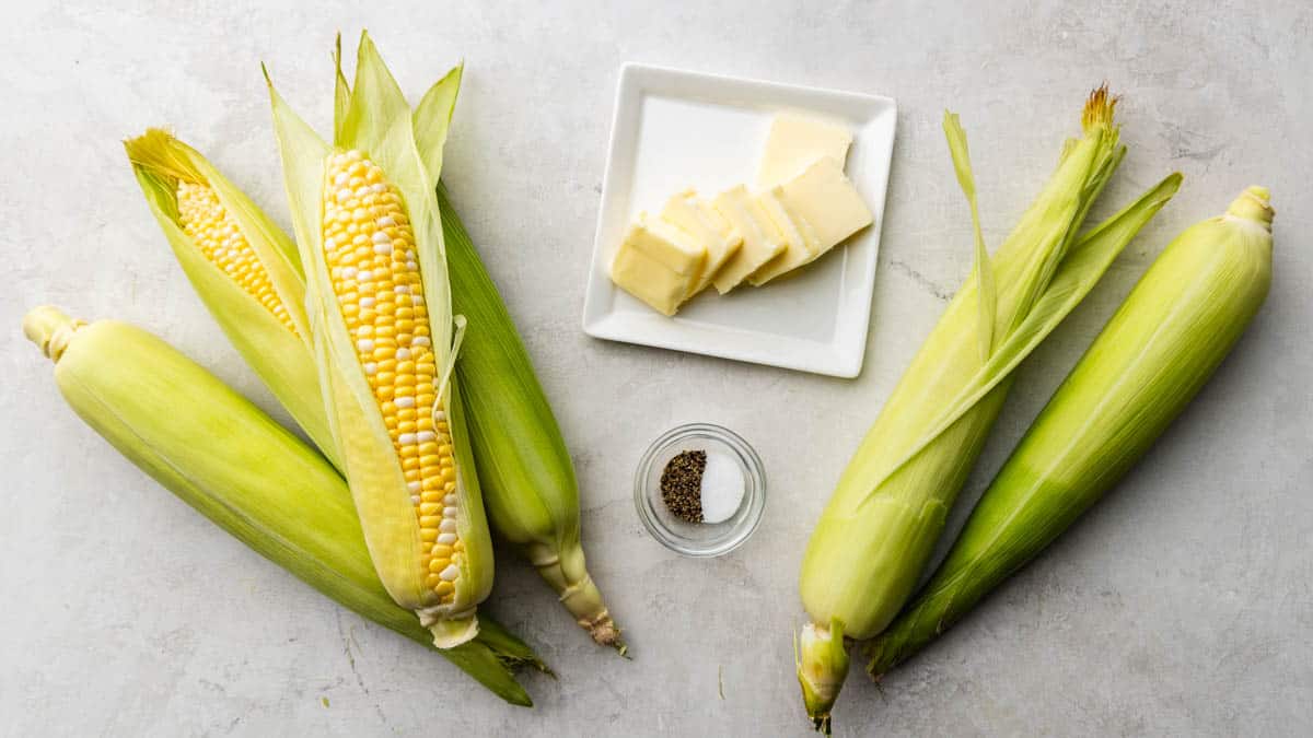Raw corn on the cob with a plate of butter and other ingredients.