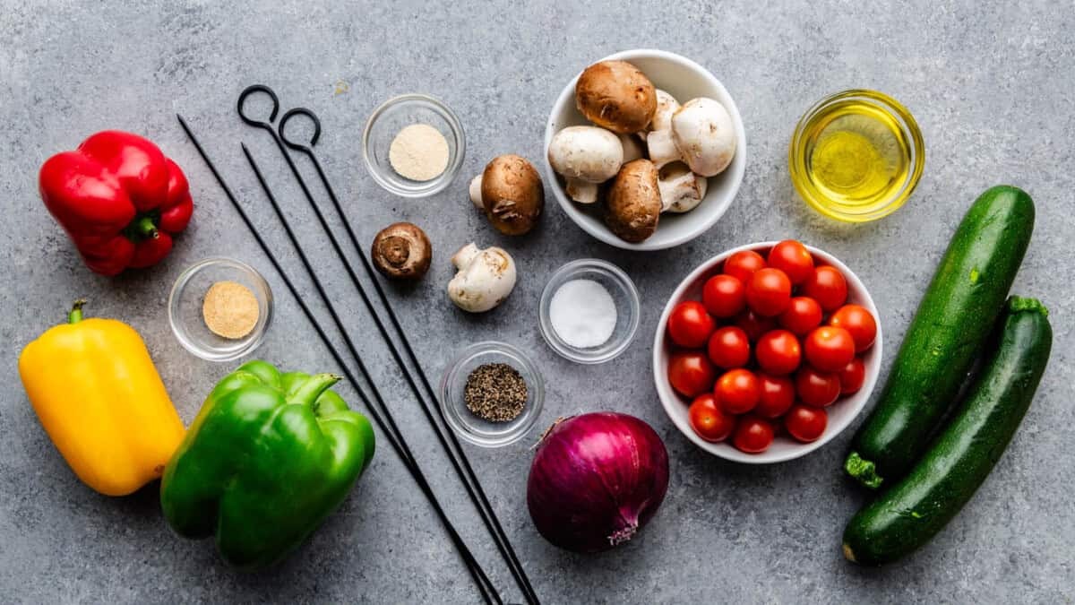 Vegetables, spices, and other ingredients for vegetable skewers arranged on a table.