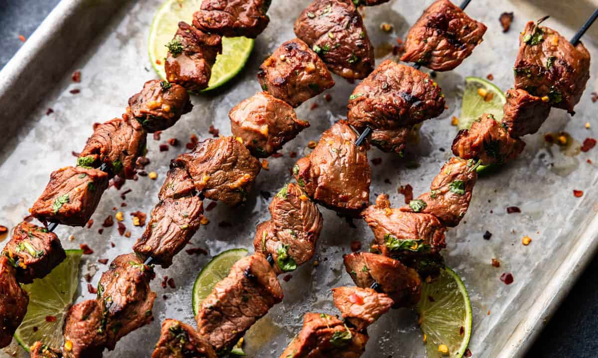 Four marinated beef kebabs are laid out on a tray.