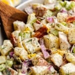 A bowl of creamy potato salad with a wooden spoon.