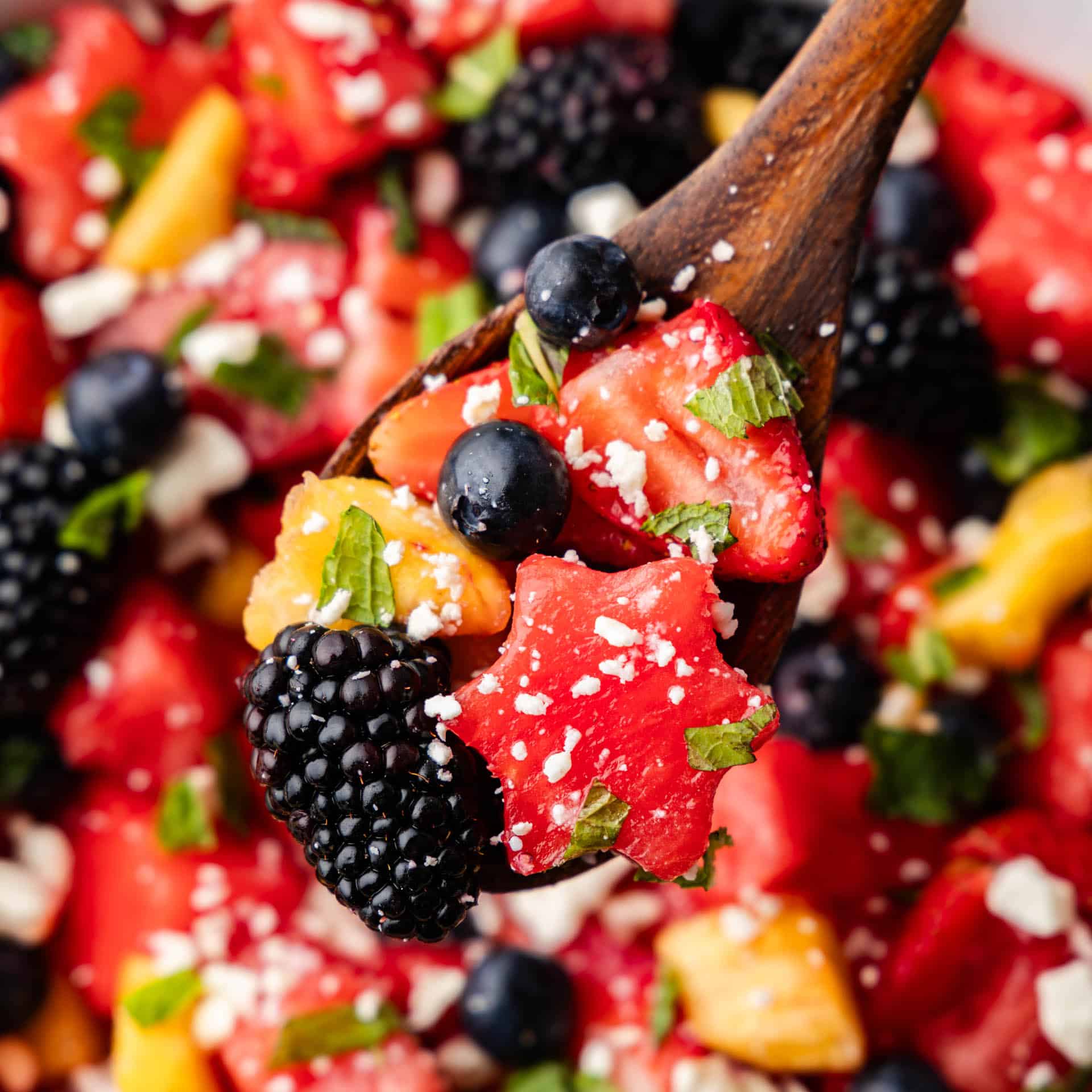 A view of red, white, and blue fruit salad with a wooden spoon.