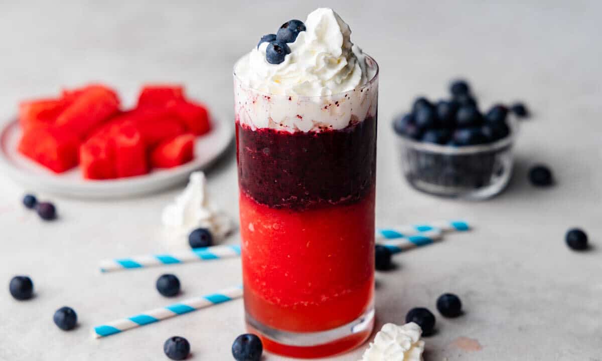 A Red, White, and Blue Slushy with watermelon and blueberries around it.