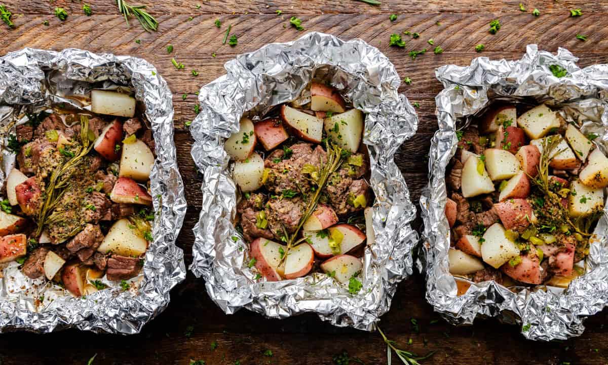 Three foil packets with cooked steak and potatoes.