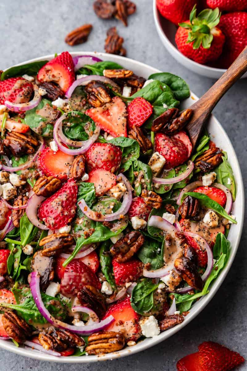 A large bowl of strawberry summer salad with a wooden spoon.