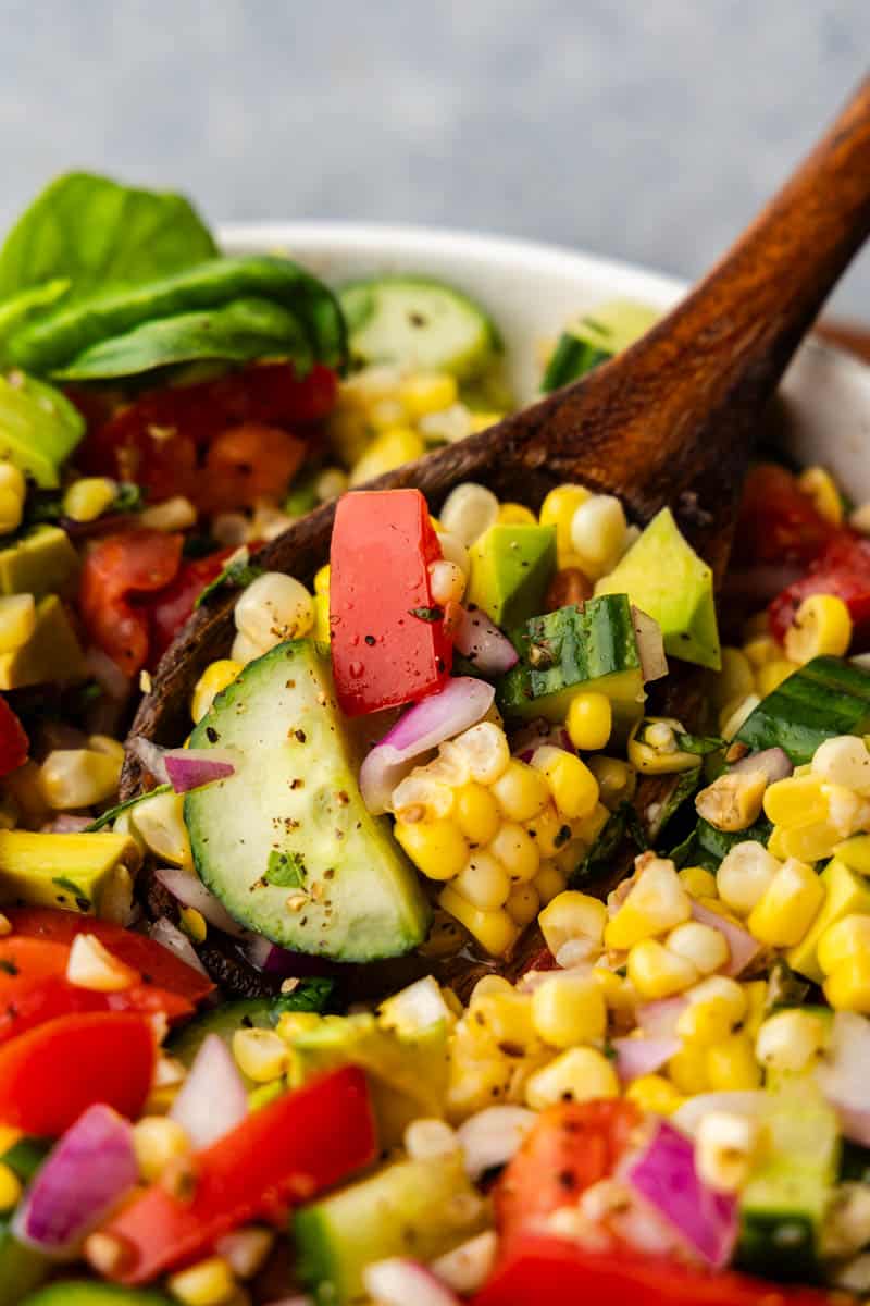 Close-up view of a bowl of fresh corn salad with zucchini, mint, tomatoes and more. 