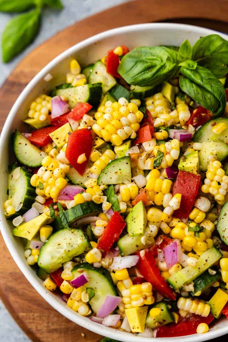 An overhead view of a bowl of corn salad with tomatoes, zucchini, onion, and herbs. 