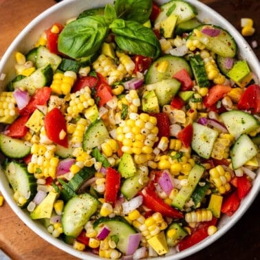 An overhead view of a bowl of corn salad garnished with fresh basil leaves.
