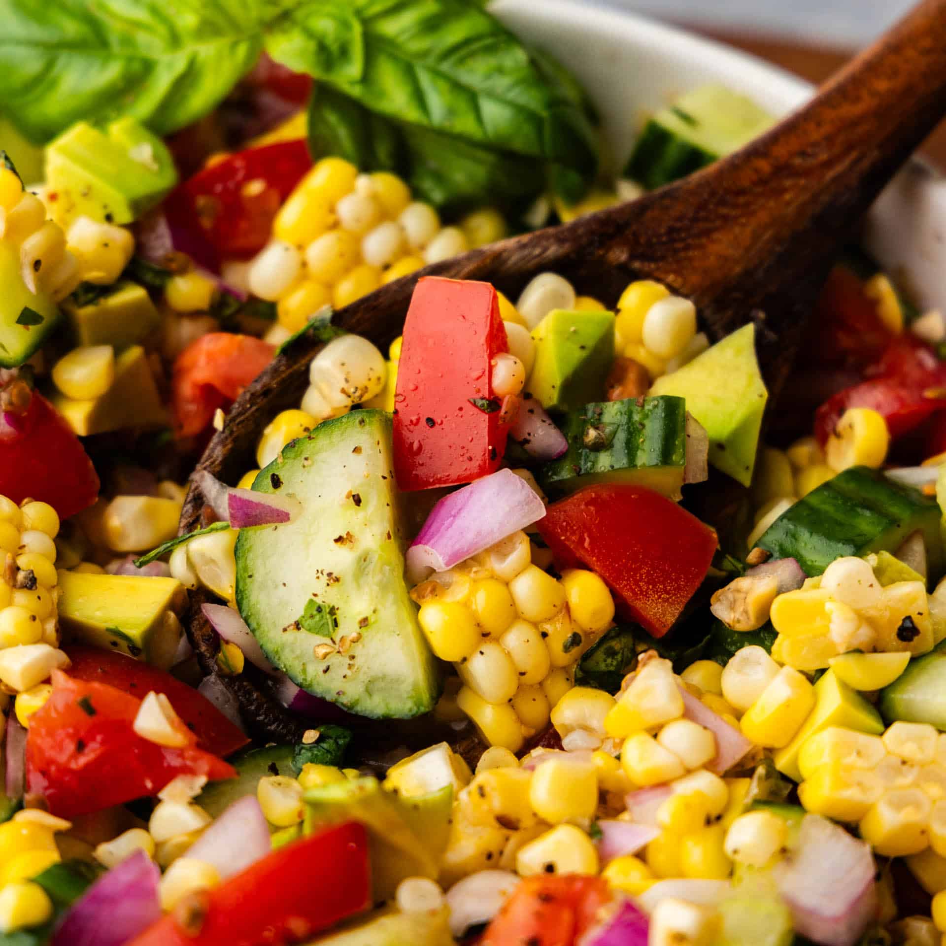 A close up view of a wooden spoon dishing out a helping of corn salad from the bowl.