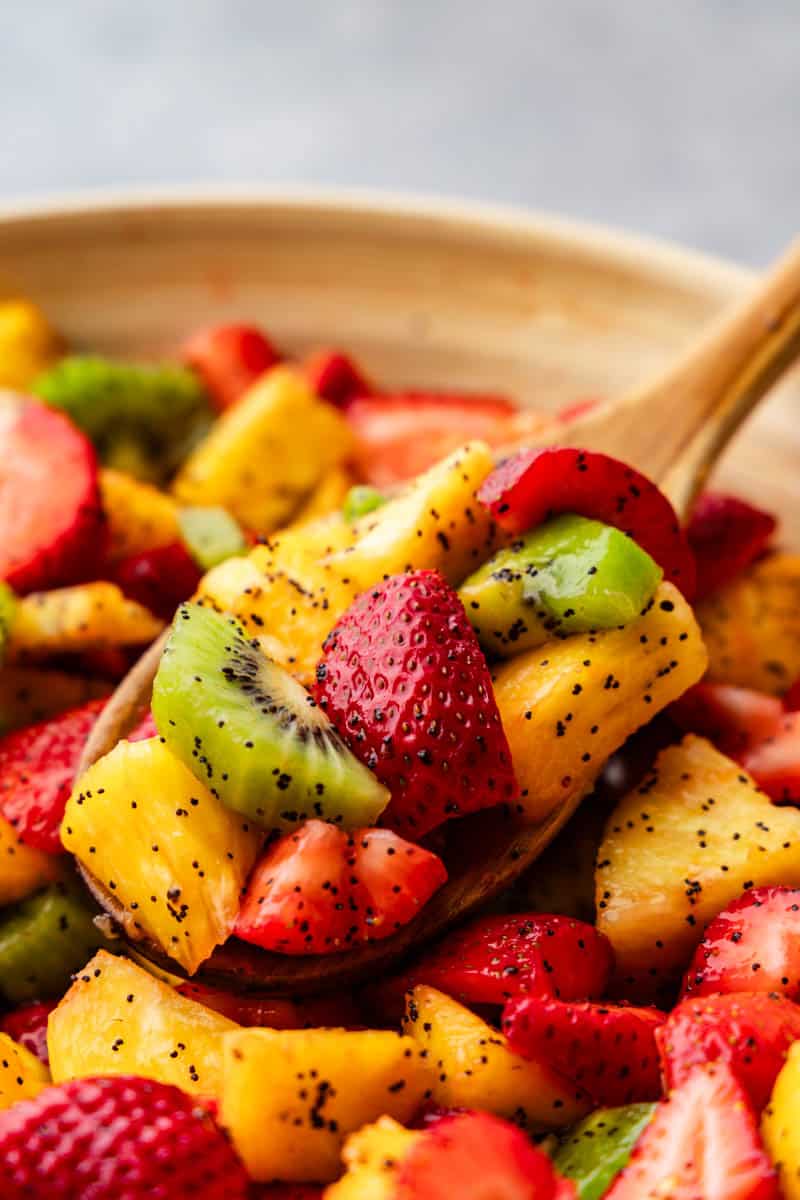 A close up view of a wooden spoon dishing out fruit salad from a bowl. 