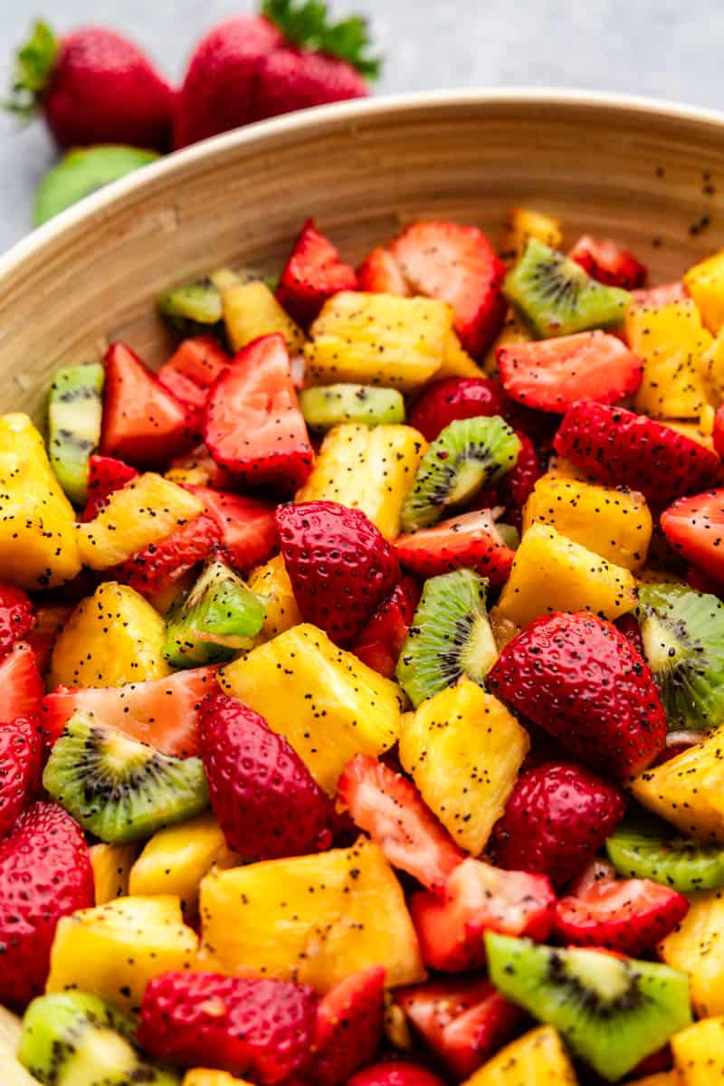 A bowl of fruit salad with pineapple, kiwi, strawberries, and a poppyseed dressing. 