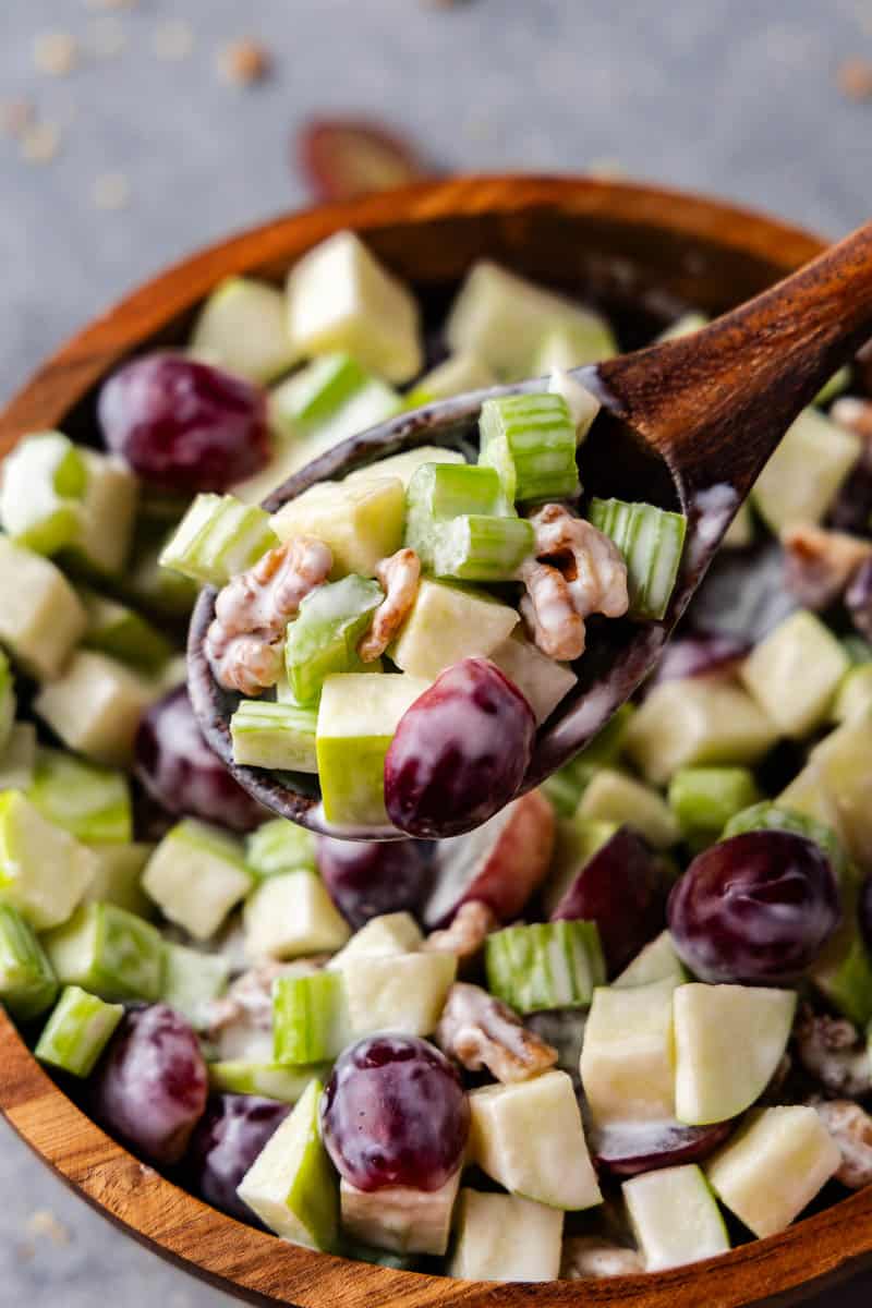 A close view of a bowl of Waldorf Salad with a wooden spoon.