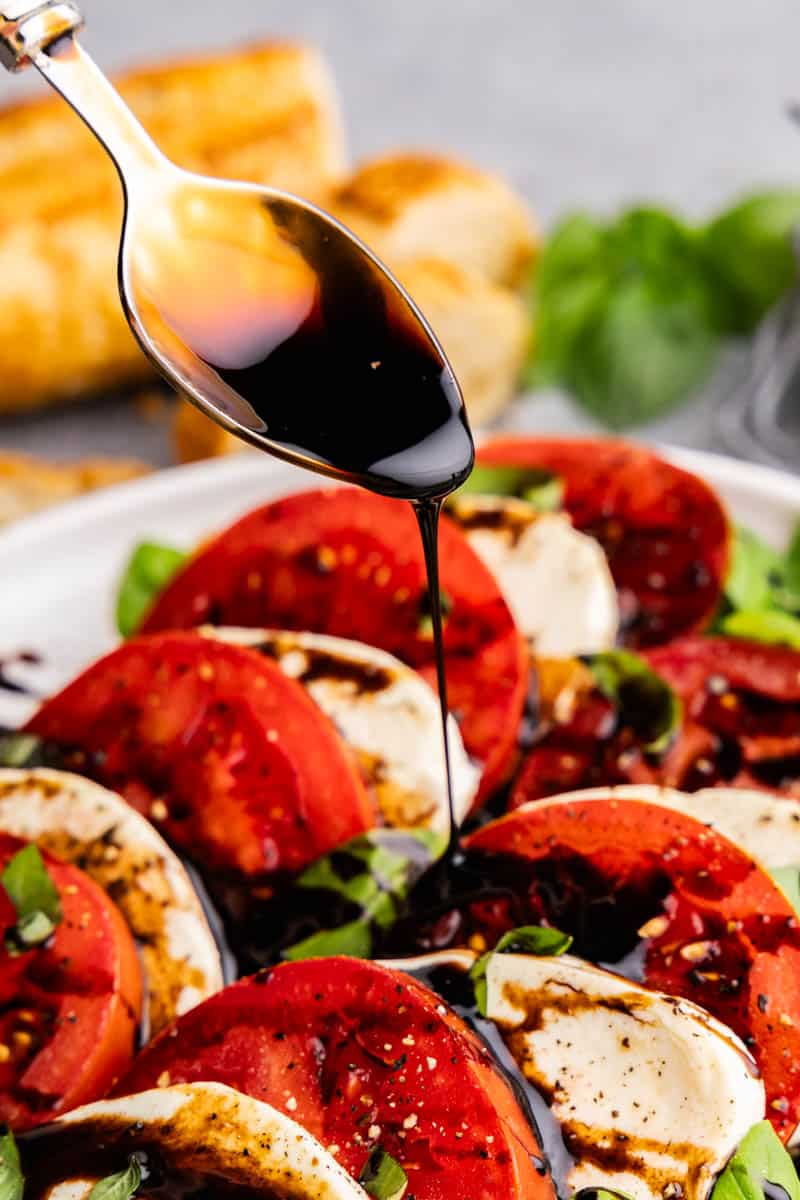A spoon drizzling balsamic glaze on top of Caprese salad.