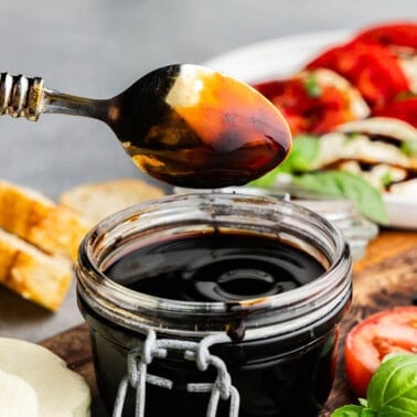 A small jar of balsamic glaze with Caprese salad and bread.