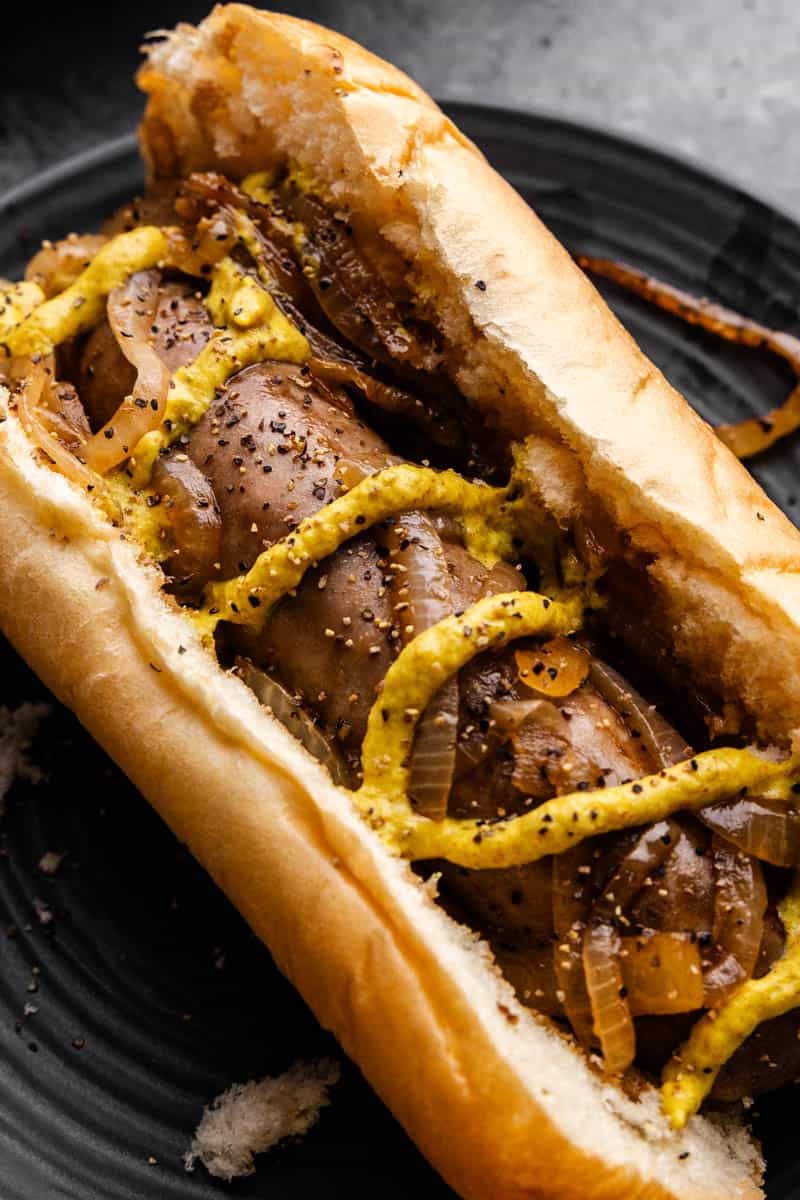 A close up overhead view of a beer braised bratwurst in a bun with onions and topped with mustard.