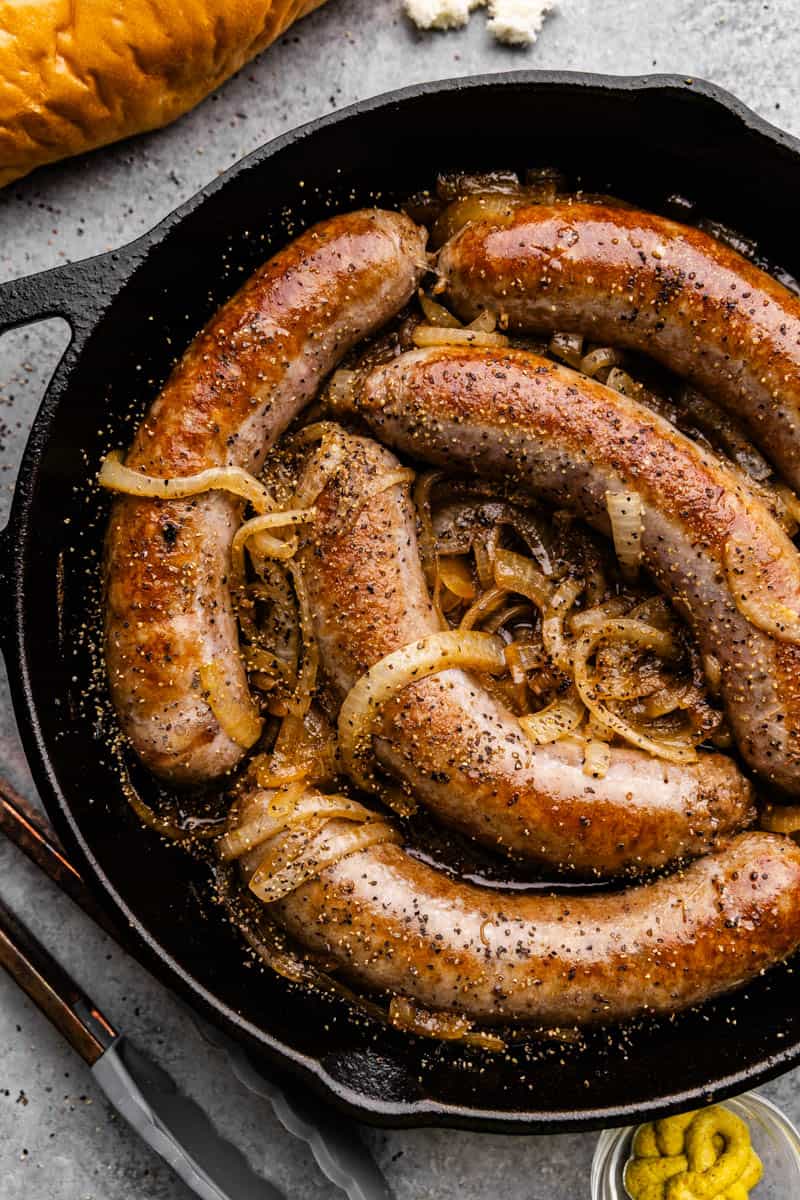 Overhead view of a cast iron skillet filled with beer braised bratwurst and onions.