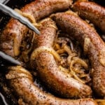 Bratwursts in a cast iron skillet that have been braised in beer with onions.