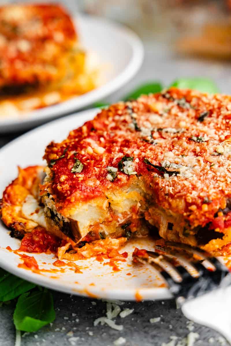 A close up view of a serving of eggplant parmesan on a plate that has been cut into so you can see the tender eggplant inside.