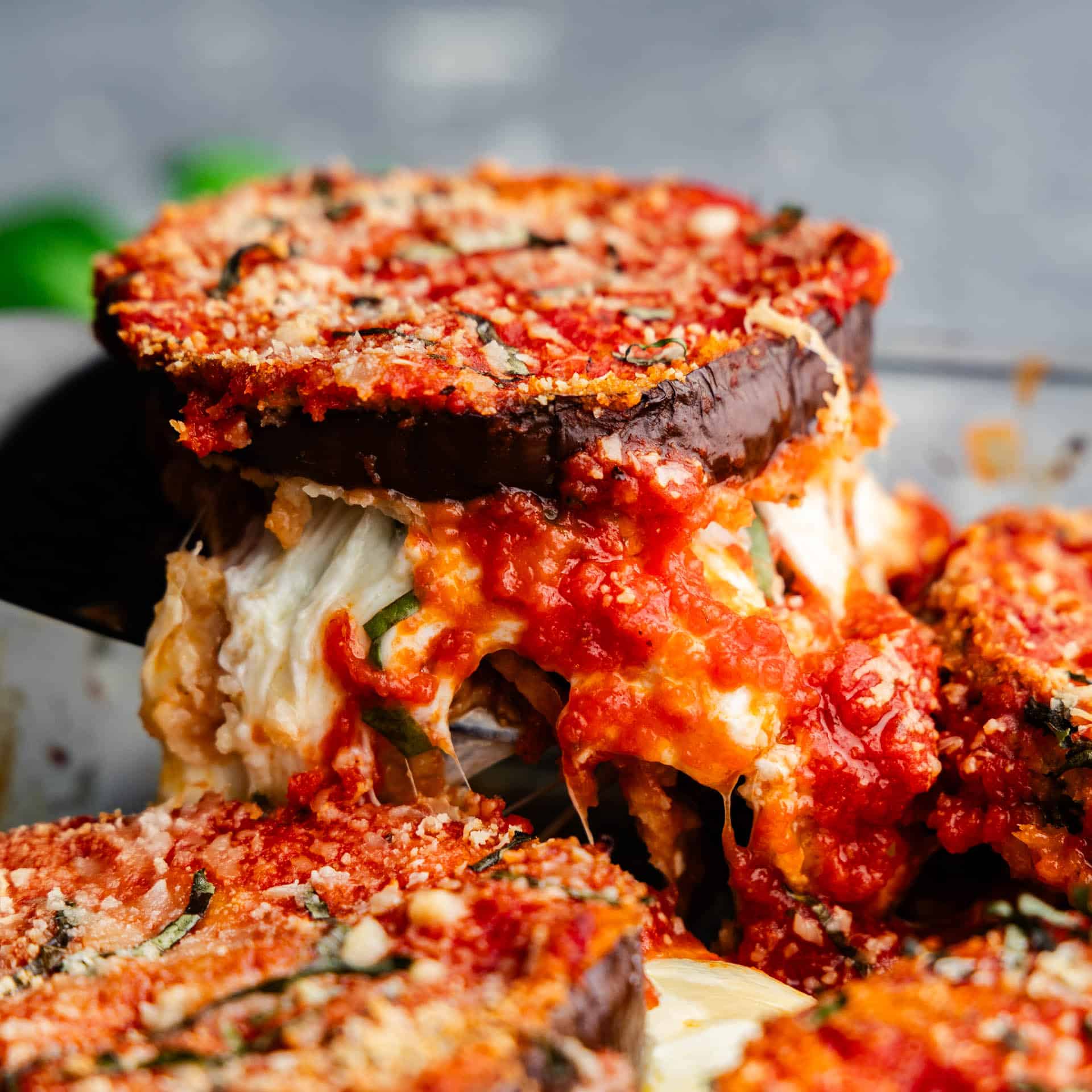 A serving of eggplant parmesan being lifted out of the pan with gooey strings of cheese.