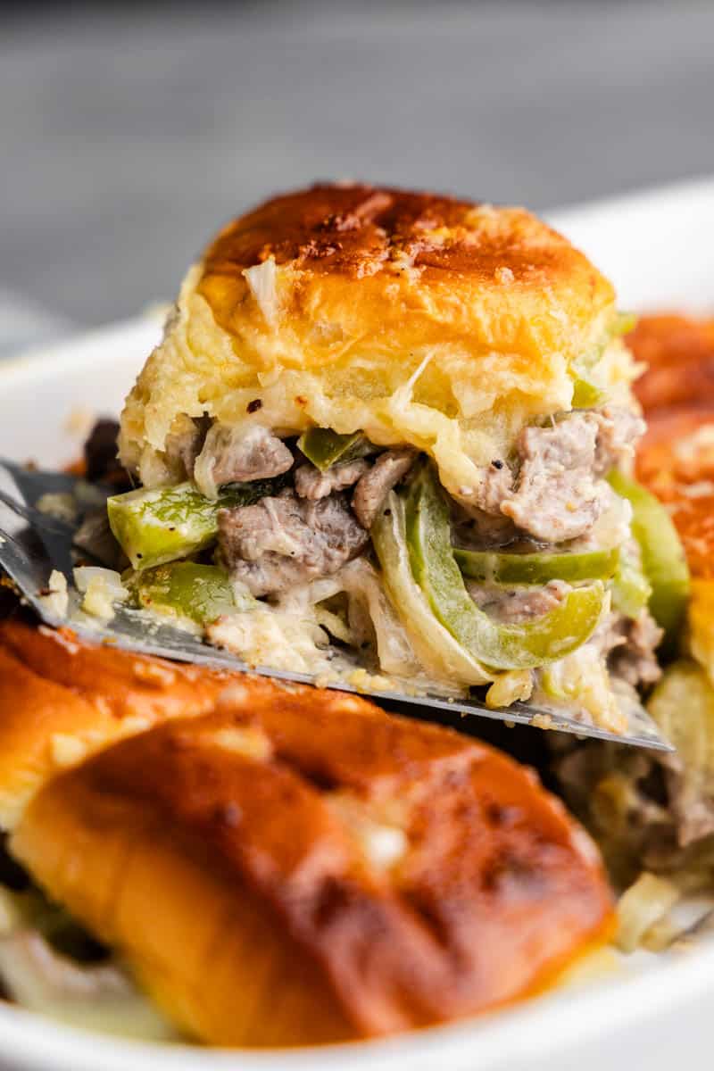 A close up view of a Philly cheesesteak slider being lifted out of the pan.