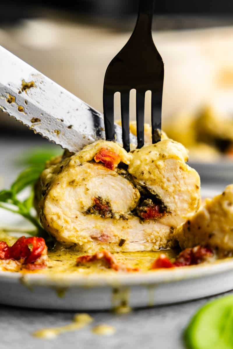 Close up view of pesto chicken roll up on plate cut with fork and knife.