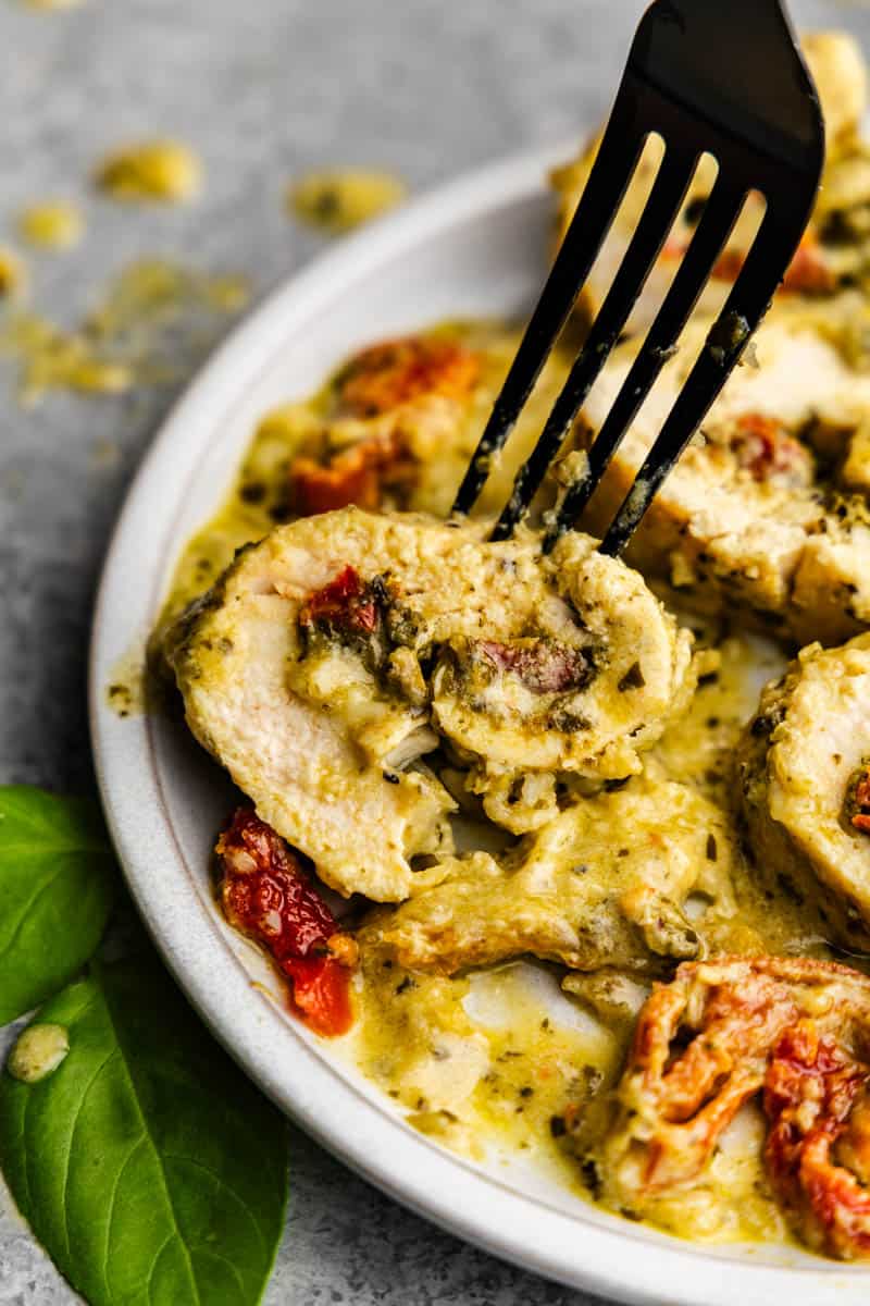 A slice of pesto chicken roll up on a plate with a fork ready to serve.