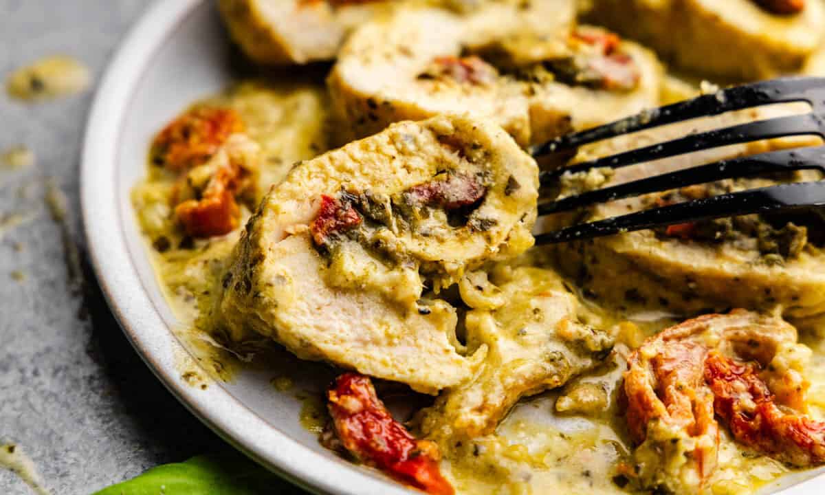 An overhead view of slices of pesto chicken roll ups on a plate in a creamy pesto sauce with sun-dried tomatoes.