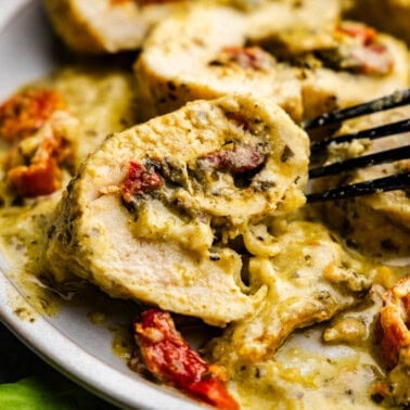 An overhead view of slices of pesto chicken roll ups on a plate in a creamy pesto sauce with sun-dried tomatoes.