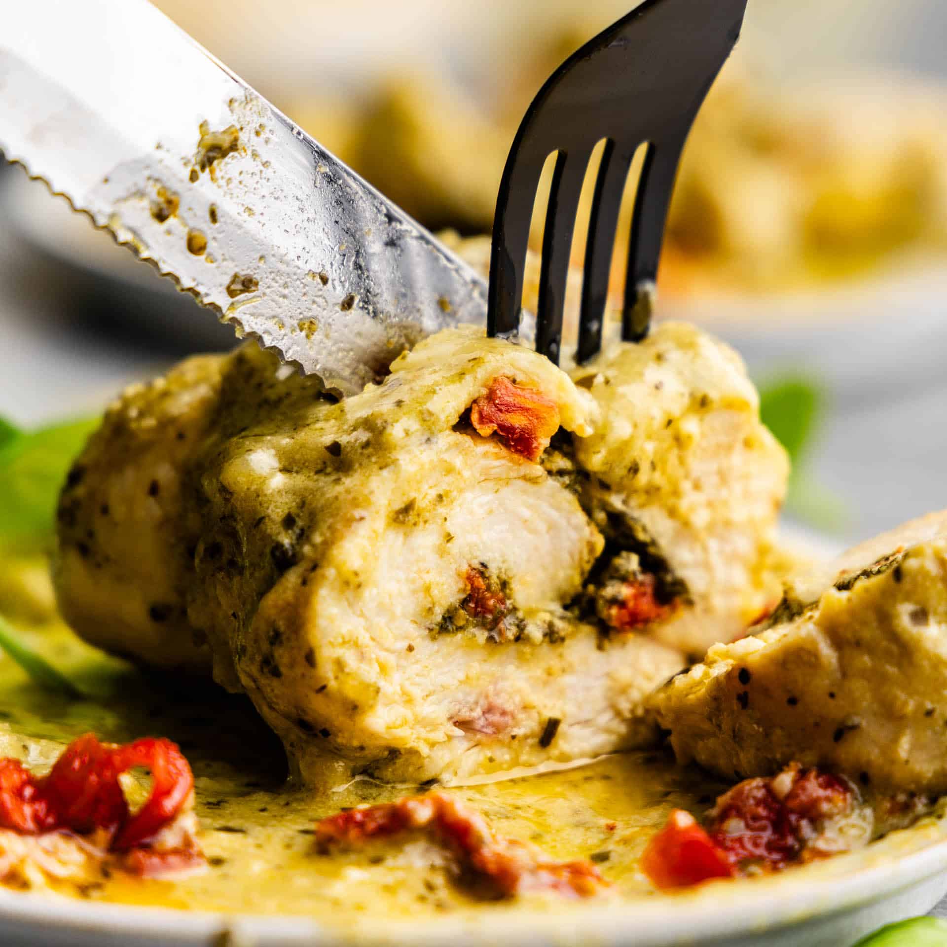 A fork and knife slicing into a pesto chicken roll up.