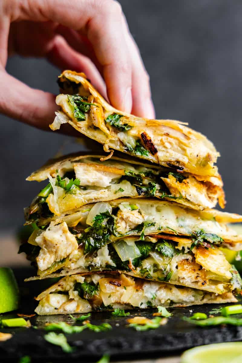 A hand lifts the top slice from a stack of cilantro lime chicken quesadillas.