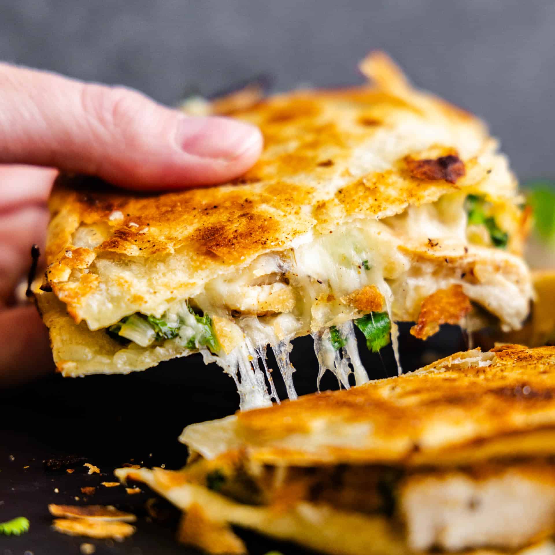 A cilantro-lime chicken quesadilla being pulled up with strings of gooey cheese.