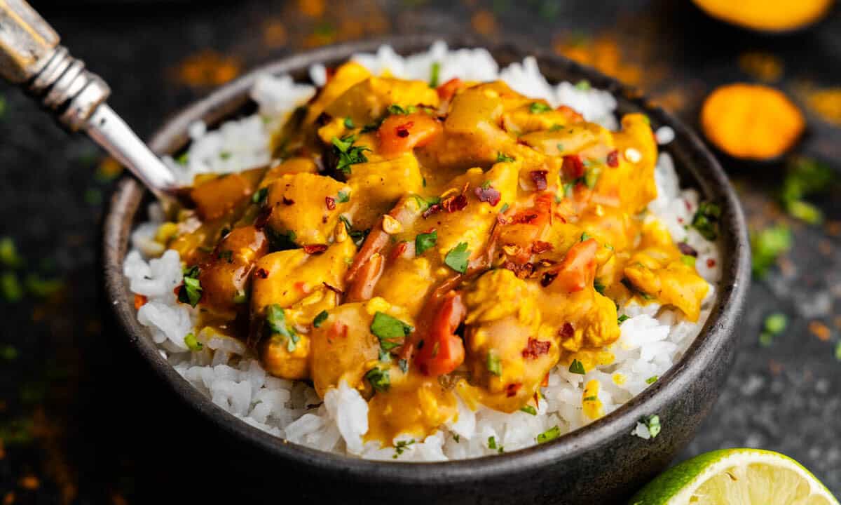 A bowl of white rice topped with coconut curry chicken.