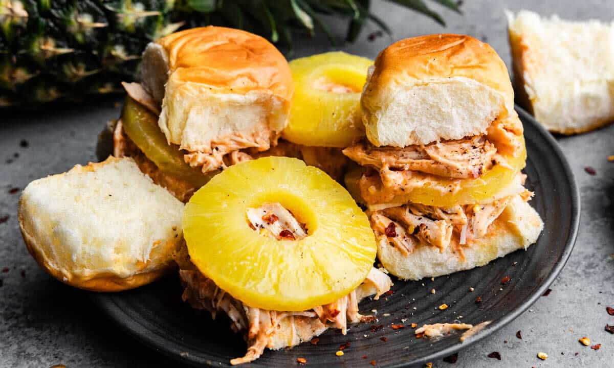Cream cheese chicken sliders on a black plate. Some of them are open-faced to see the sliced pineapple in each slider.